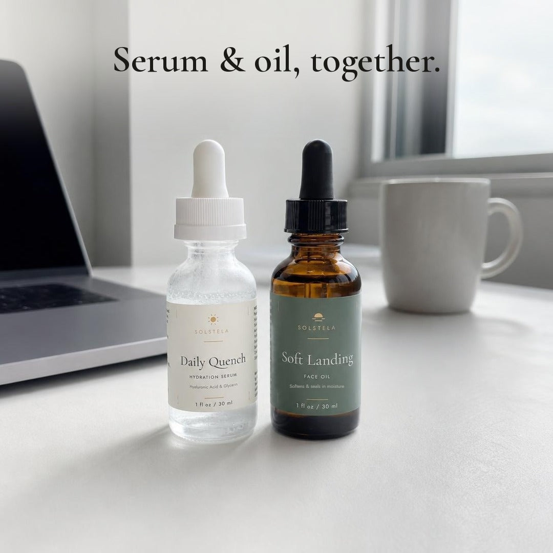 Serum and oil, together: Daily Quench and Soft Landing side by side on an office desk by a window, with a laptop and a mug