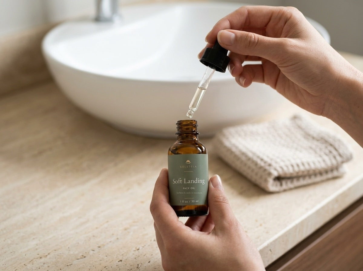 Hands drawing Soft Landing face oil into its dropper at a bathroom sink